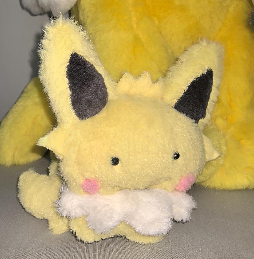 Handmade yellow Eeveelution plush sewn from the pattern, photographed with large plush toys in the background