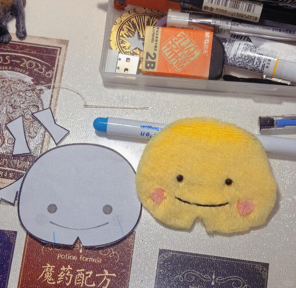 Handmade yellow plush toy sample with pink cheeks and embroidered smile, shown beside a paper pattern template during the sewing process