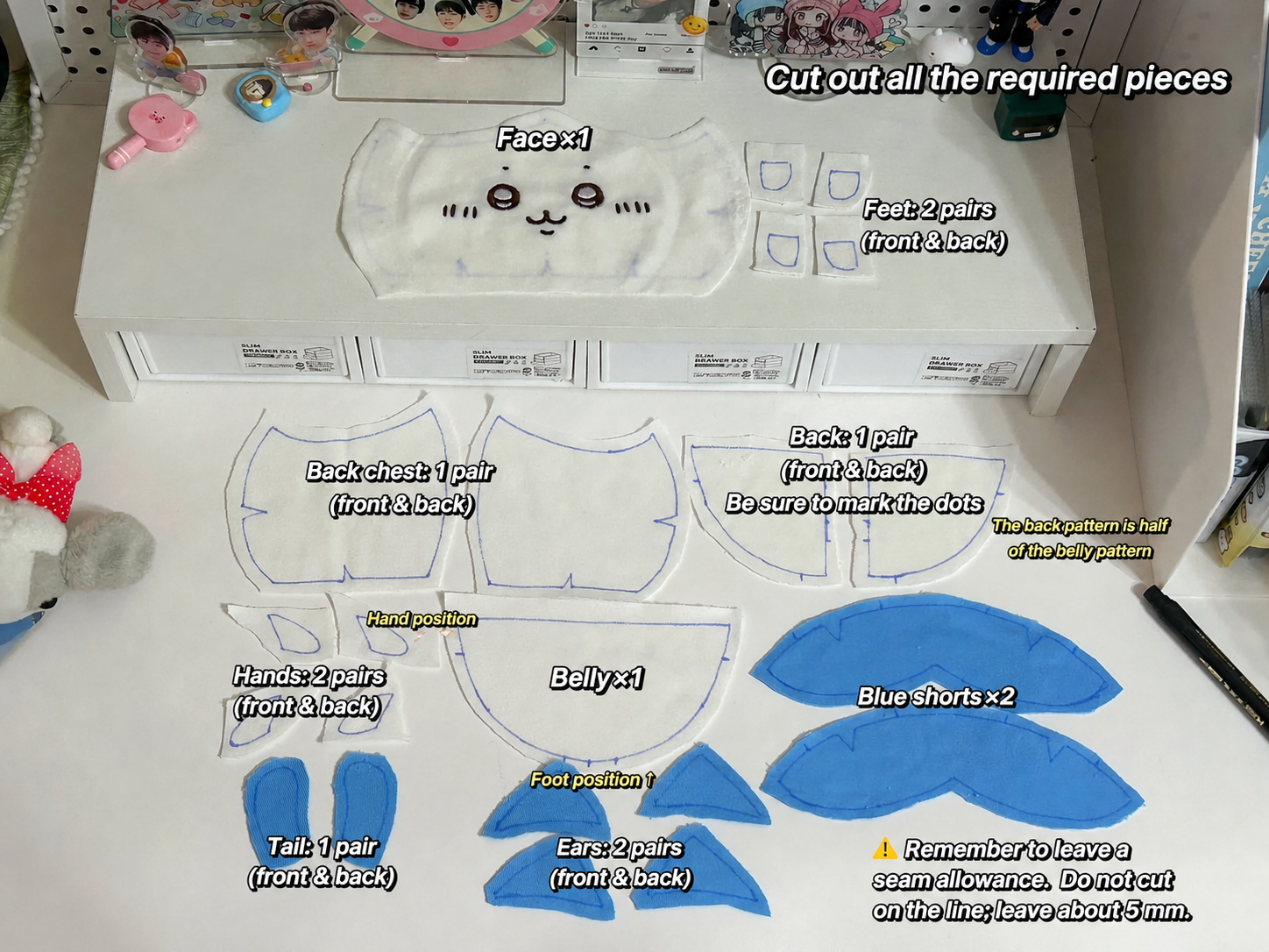 A flat lay of embroidered petal-shaped fabric pieces for a cat face and body applique, laid out on a white desk with printed cut lines and handwritten labels indicating piece counts and positions.