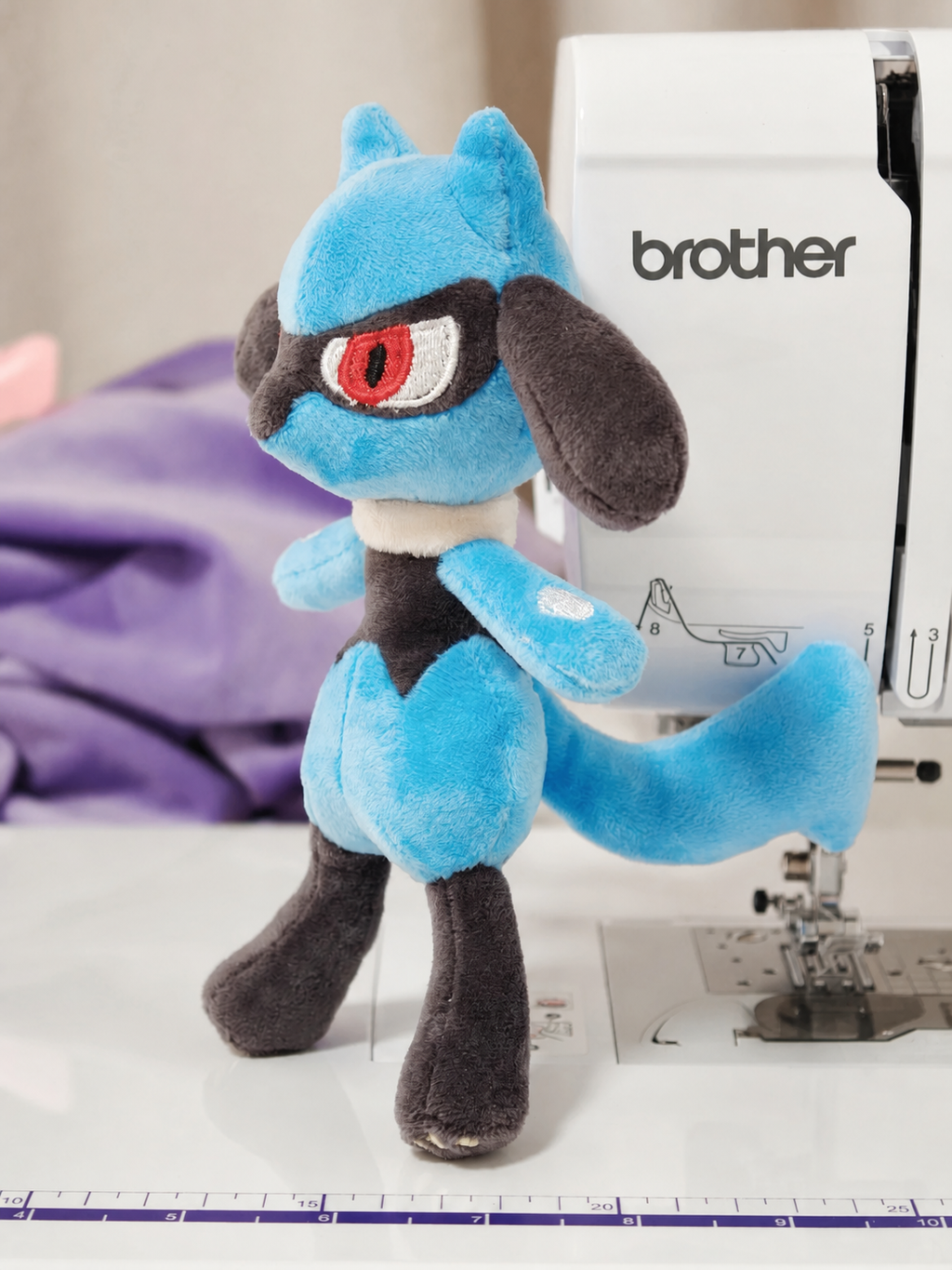 Handmade blue and black Lucario-inspired plush beside a sewing machine, created from the printable PDF sewing pattern
