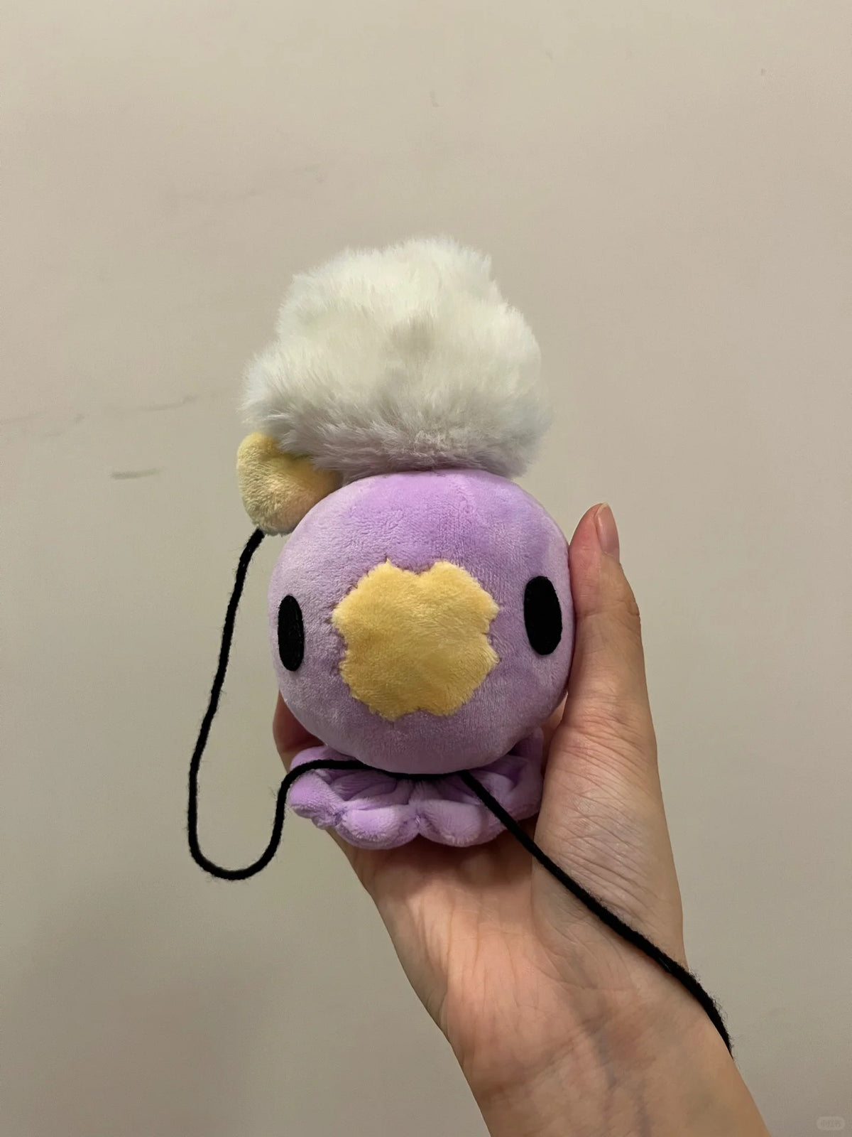 Palm-sized lavender Drifloon plush with appliqué face and dangling black cords