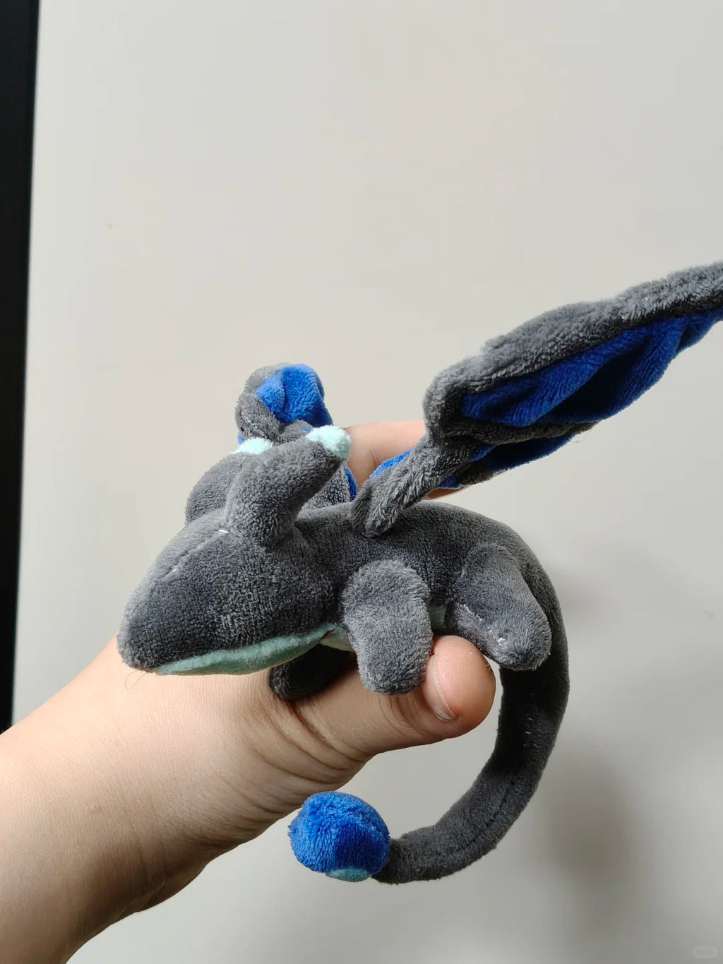Side view of a four-legged palm dragon plush with blue wings and curved tail
