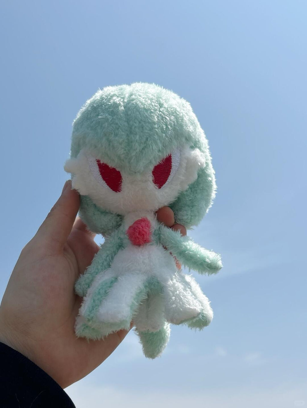 Handmade mint green Gardevoir plush doll held against a clear blue sky