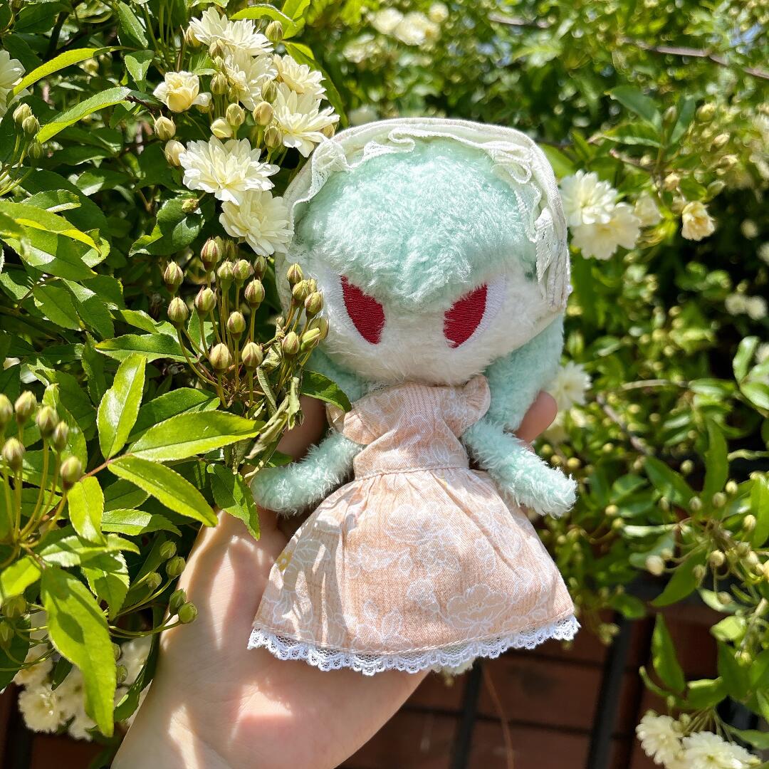 Handmade Gardevoir plush doll wearing a peach floral dress and lace headpiece among white flowers
