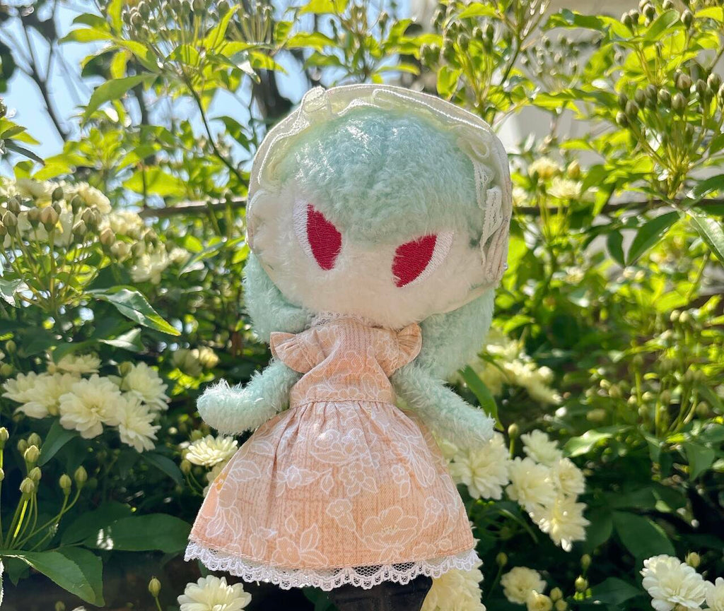 Finished handmade Gardevoir plush doll in a peach floral dress photographed in a sunny garden