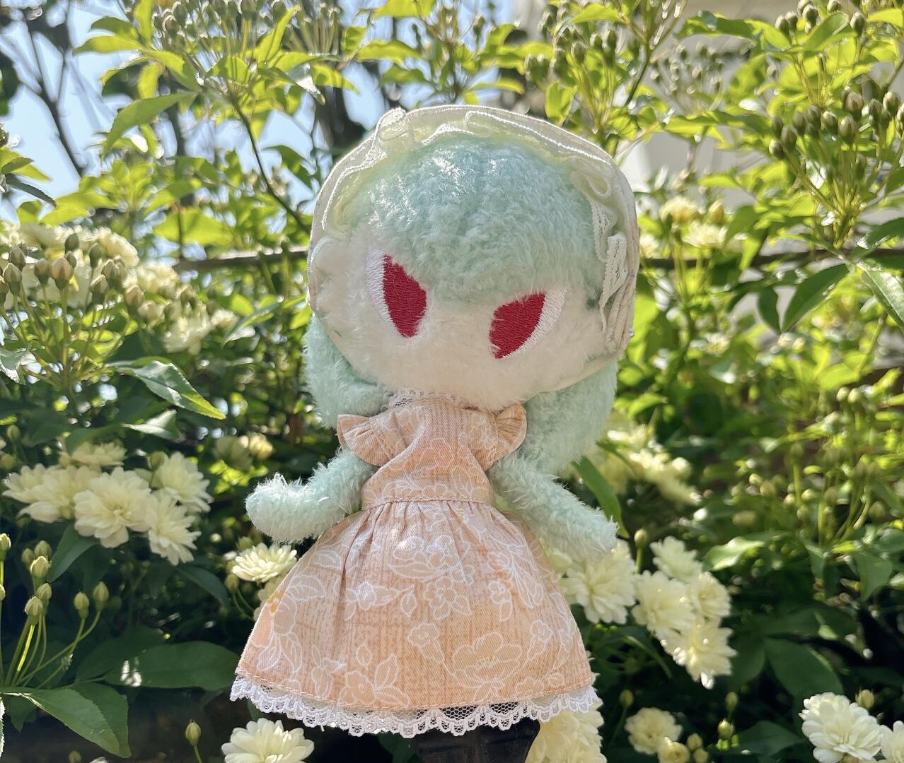 Finished handmade Gardevoir plush doll in a peach floral dress photographed in a sunny garden