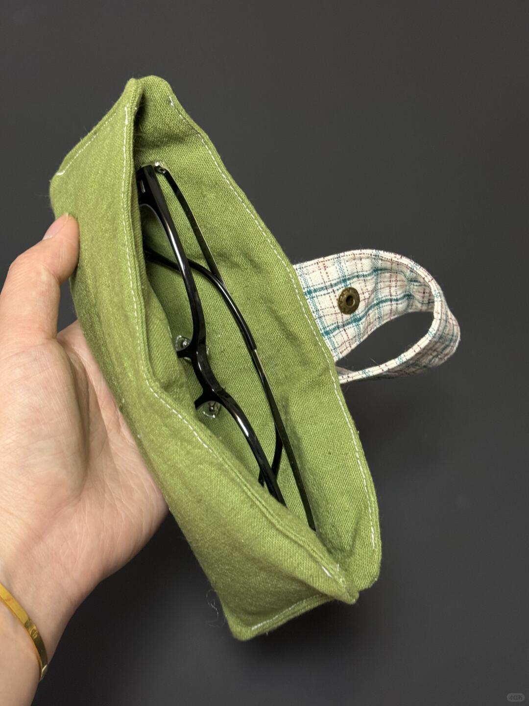 Green fabric pouch with glasses held by a hand against a dark background