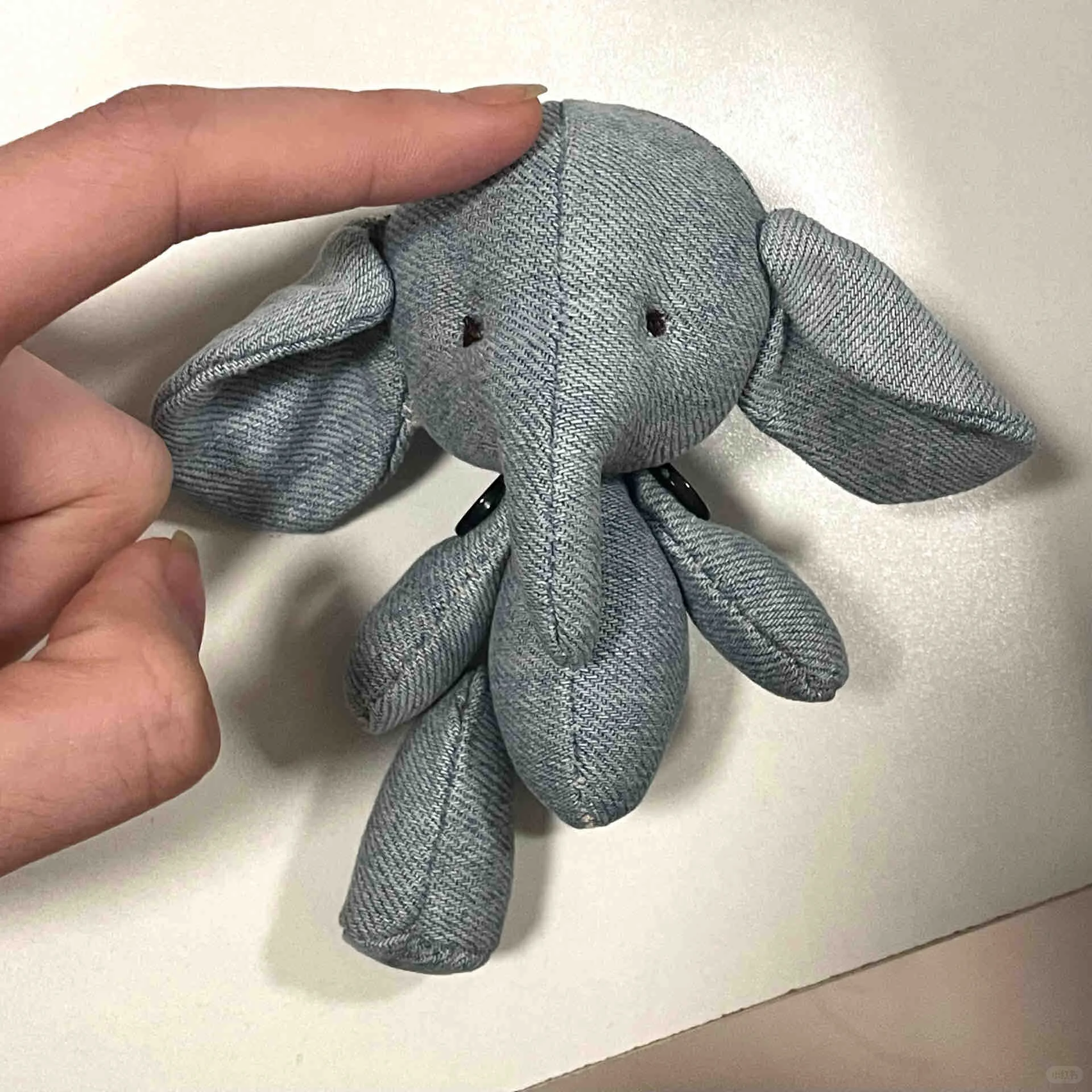 Close-up of a small handmade grey elephant plush beside a person's hand for scale