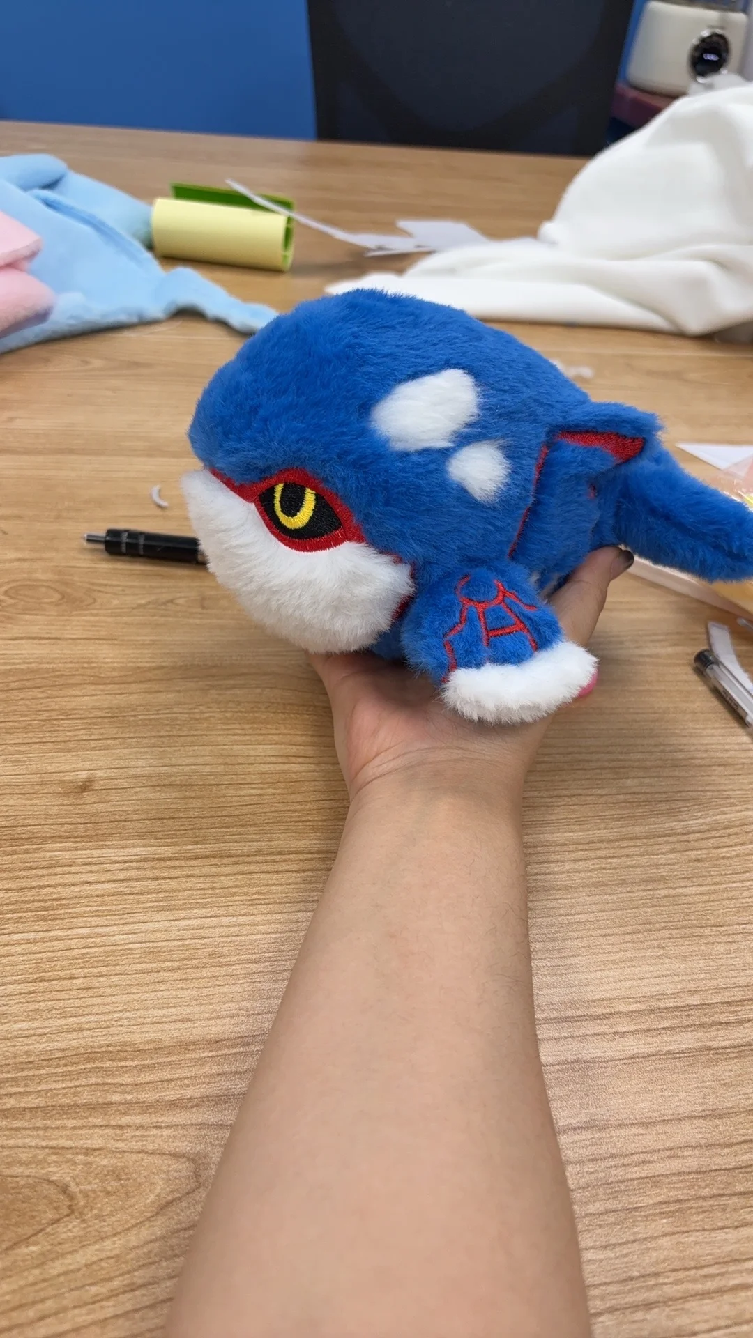 Handmade medium blue Kyogre plush held above a sewing workspace