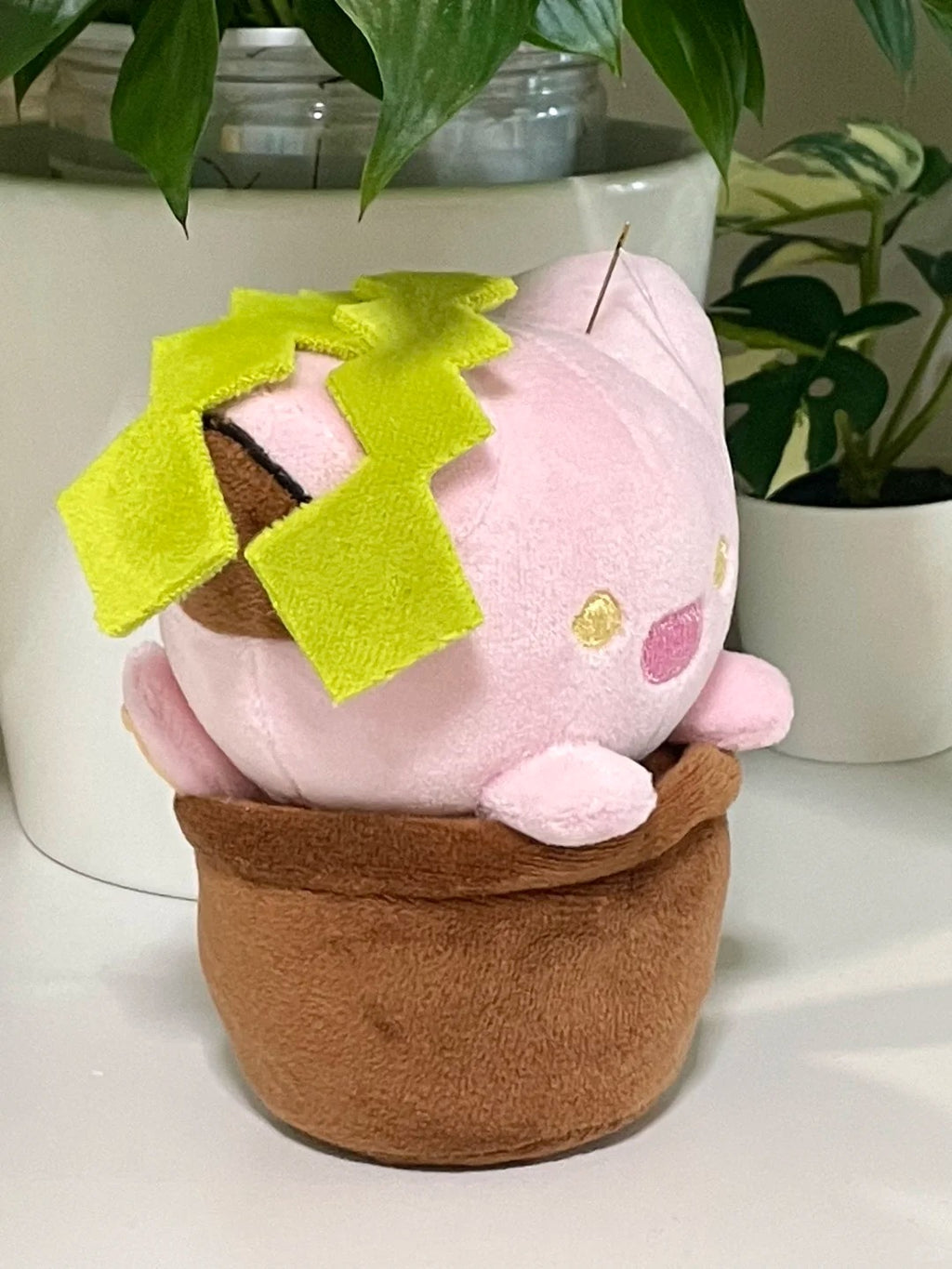 Side view of a pink cat plant plush sitting in a brown fabric flowerpot