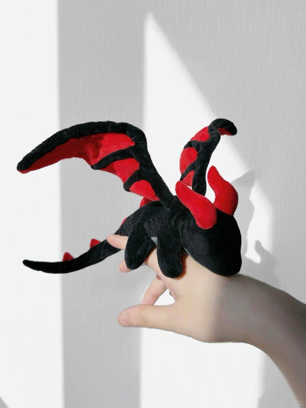 Black and red dragon-shaped plush toy held by a hand against a white background