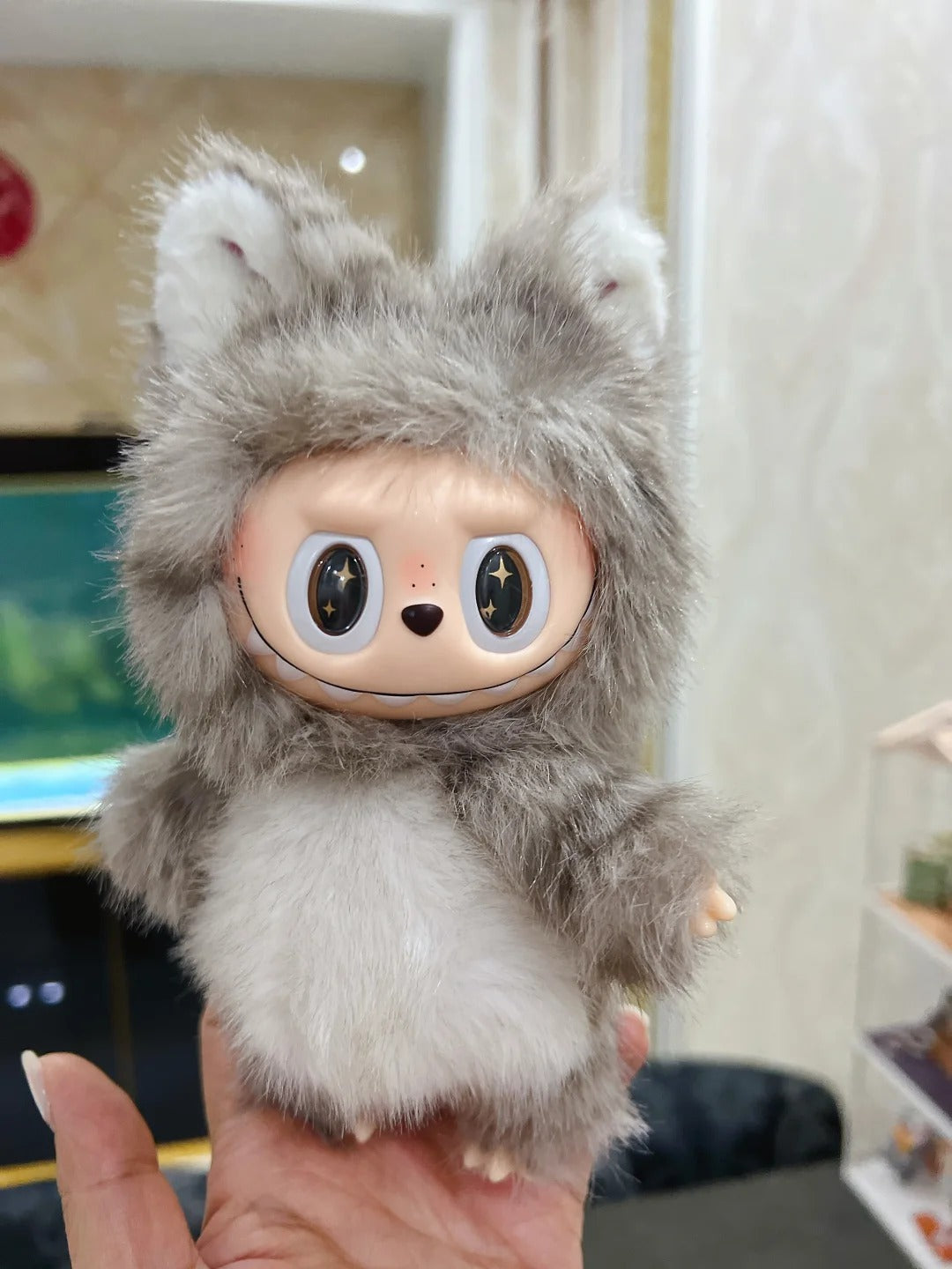 Plush toy with a labubu cat furry exterior and face with large eyes held by a hand.