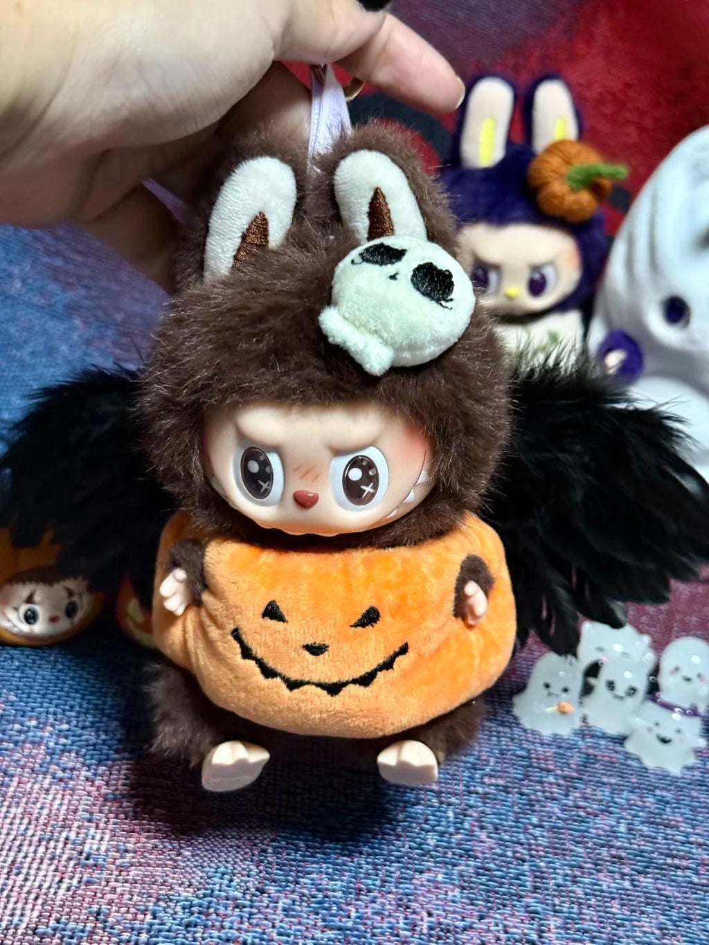 Halloween-themed plush toy with bat wings and pumpkin face on a textured surface