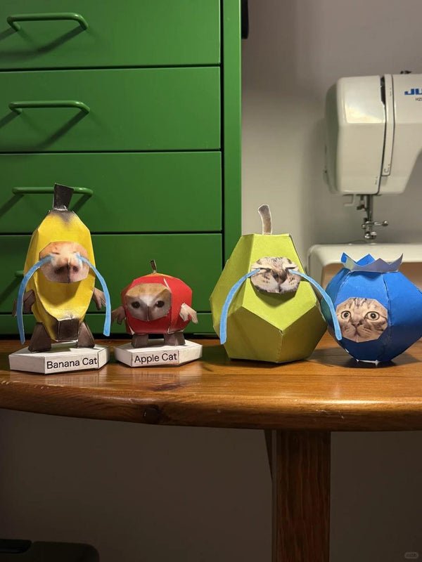 Four meme cat objects on a wooden surface with a green cabinet and sewing machine in the background.