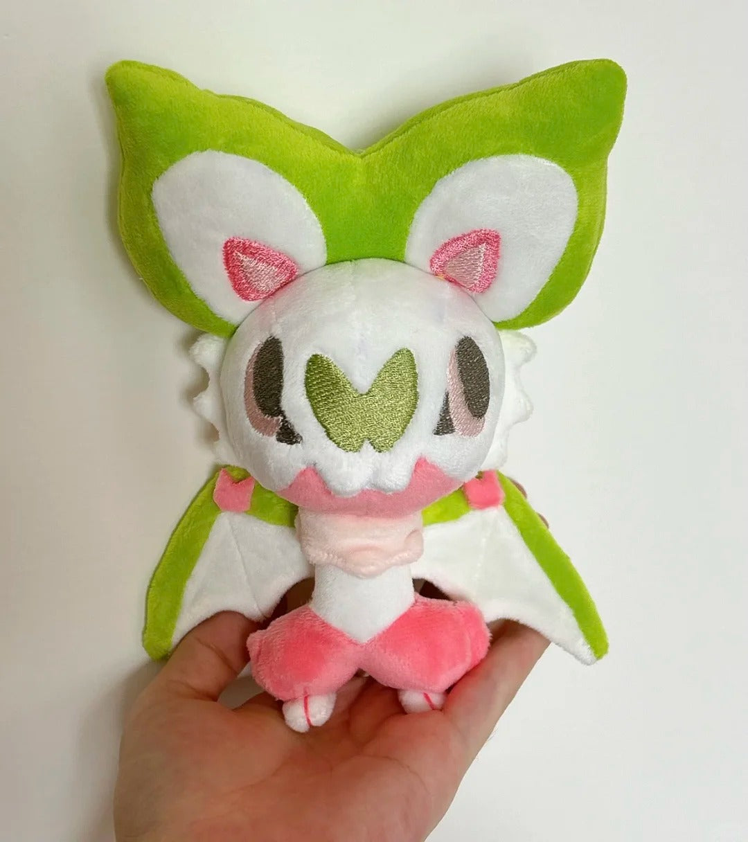 Front view of a handmade green pink and white Noibat plush with large ears and open wings