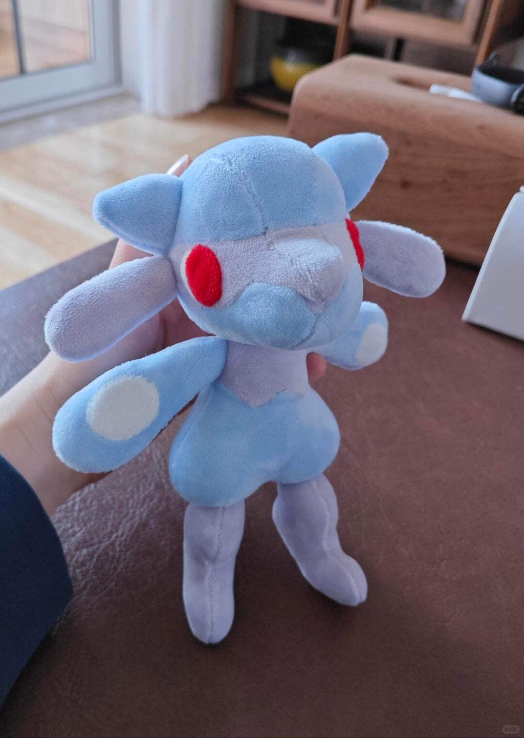 Handheld light blue Lucario-inspired plush prototype with red eye details and soft grey accents