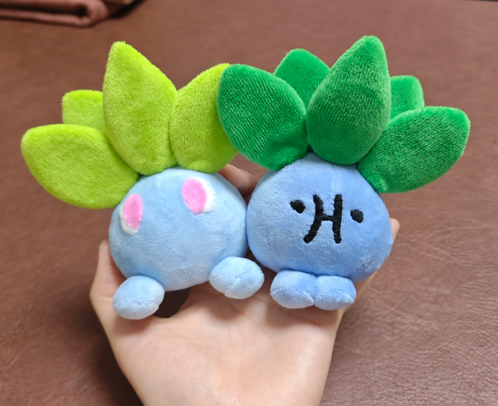 Two handmade blue Oddish plush toys with green leaves held in one hand