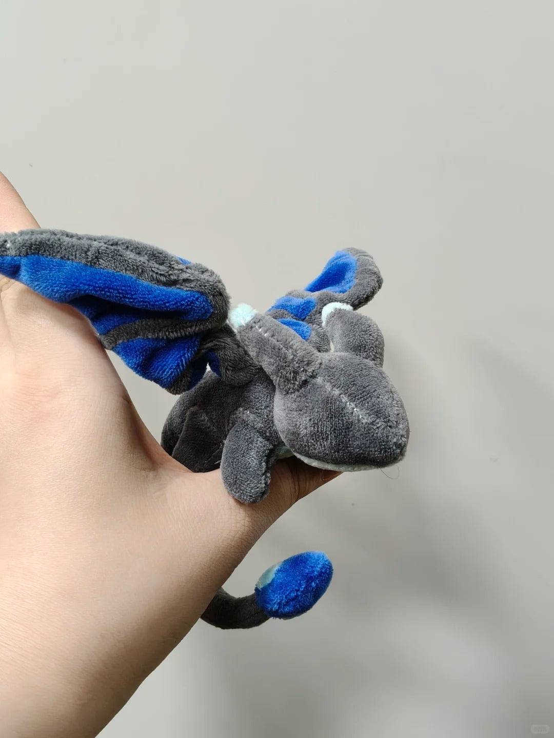 Close-up of a grey and blue palm dragon plush with folded fabric wings