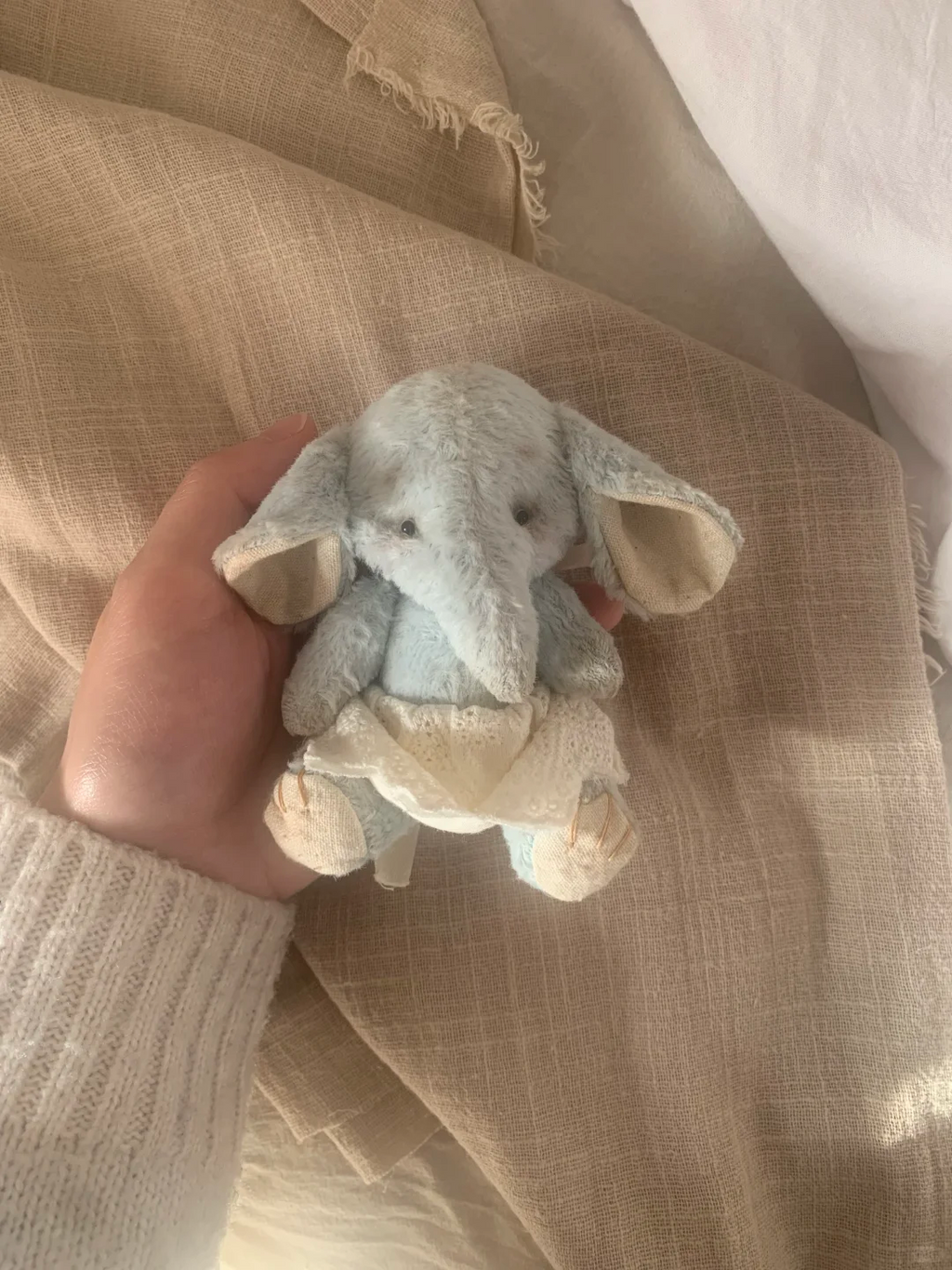 Small light blue handmade elephant plush wearing a white dress in natural sunlight