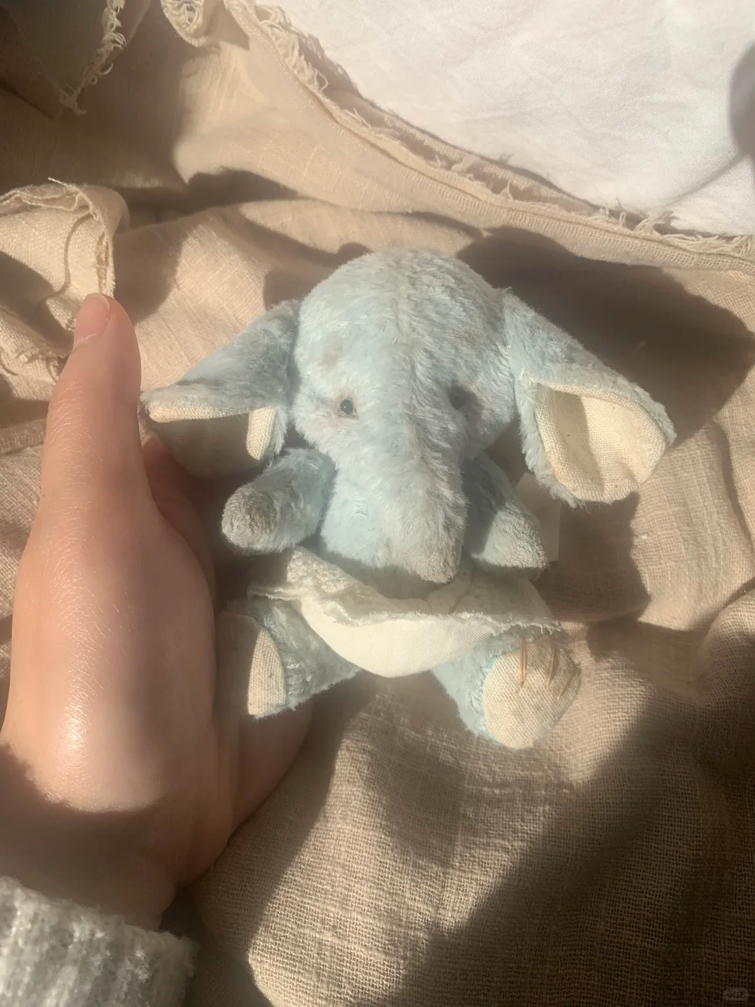 Palm-sized light blue elephant soft toy with cream ears and a white dress