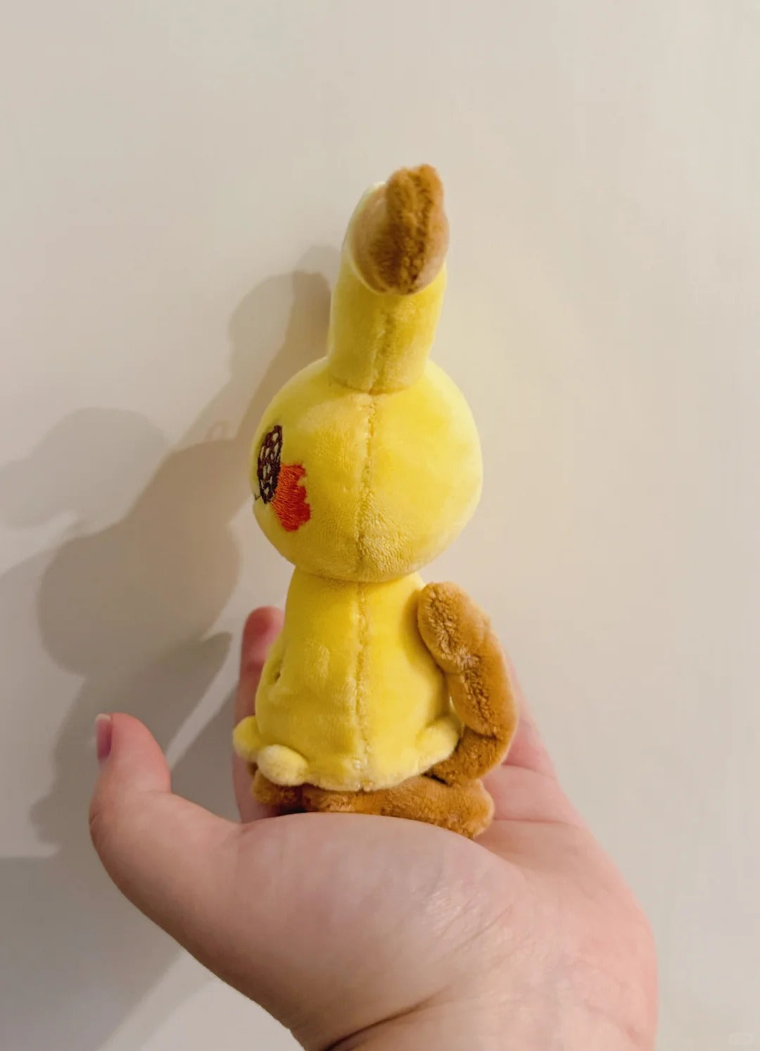 Side view of a standing Mimikyu plush with brown ear tips, tail and feet