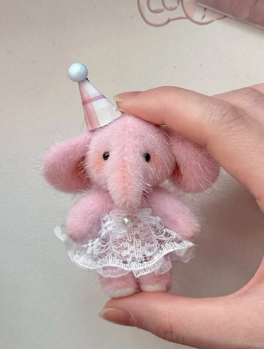 Tiny pink handmade elephant plush wearing a lace dress and party hat