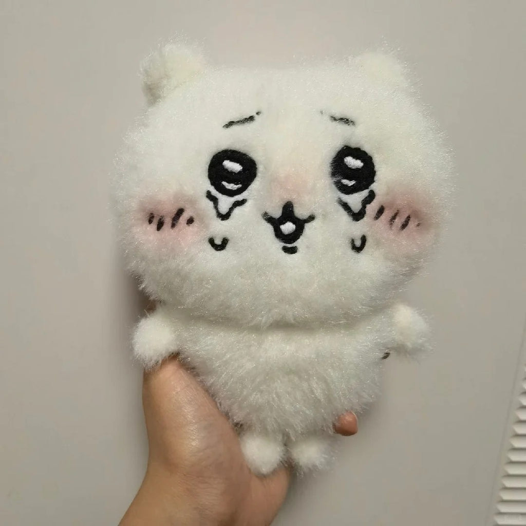 A white fluffy plush toy with a cute cartoon face, held in a person's hand against a plain indoor wall.