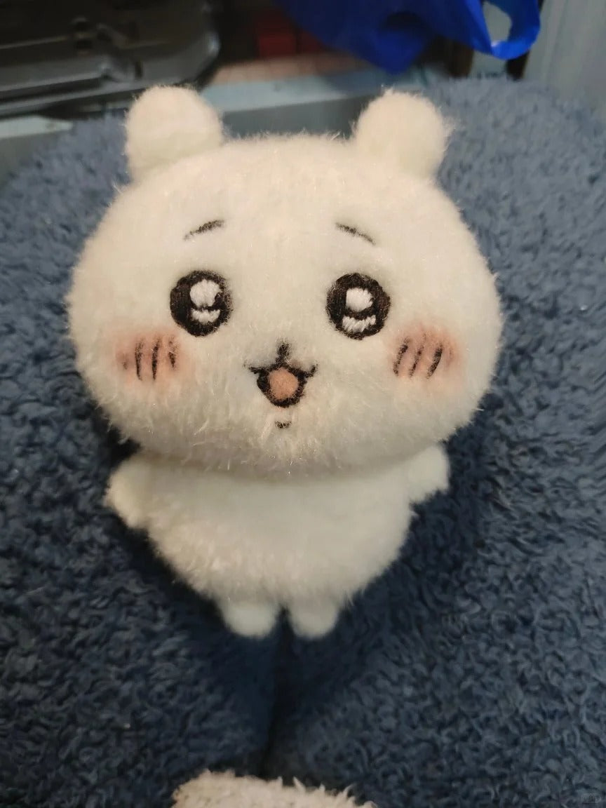 A white fluffy plush toy with a cute cartoon face, sitting on a textured blue blanket.